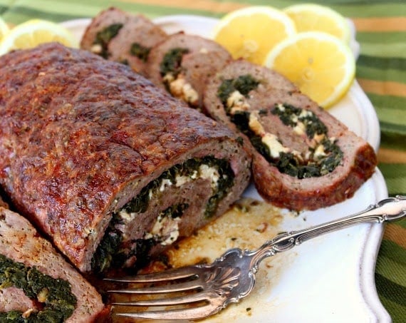 A Rolled Greek Meatloaf stuffed with spinach and feta cheese on a platter with a serving fork.