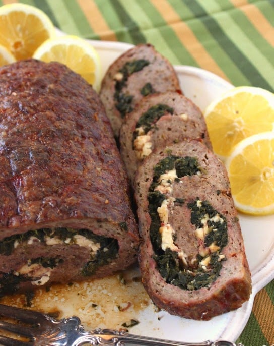 A Rolled Greek Meatloaf stuffed with spinach and feta cheese on a platter with a serving fork.