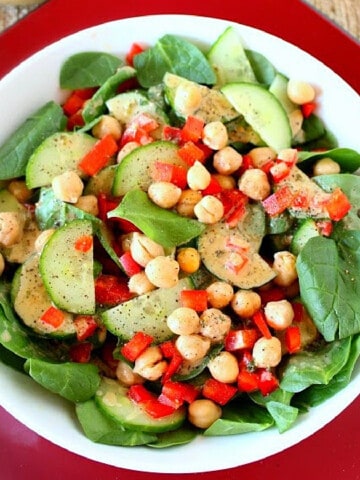 A colorful salad of Spinach, Chickpea, and Red Pepper on a white and red plate with cucumber.