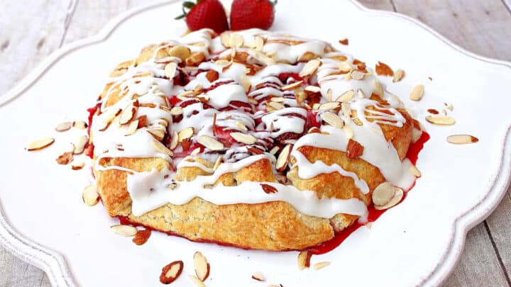 A Strawberry Crostata on a pretty white square plate with a almond glaze and sliced almonds.