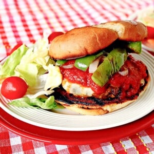 A delicious Italian Sausage Pizza Burger with sauce, peppers, and onions on a plate.