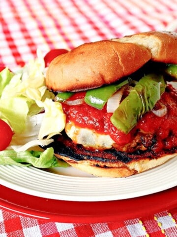 A delicious Italian Sausage Pizza Burger with sauce, peppers, and onions on a plate.