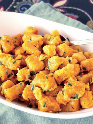 A white oval bowl filled with orange colored Butternut Squash and Potato Gnocchi and topped with chives.