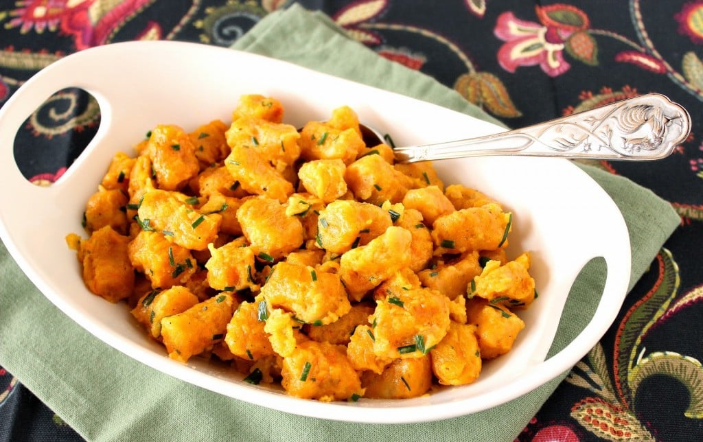 A white oval bowl filled with orange colored Butternut Squash and Potato Gnocchi and topped with chives.