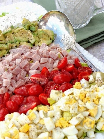 A colorful Cobb Salad with rows of egg, tomato, ham, avocado, and cottage cheese.