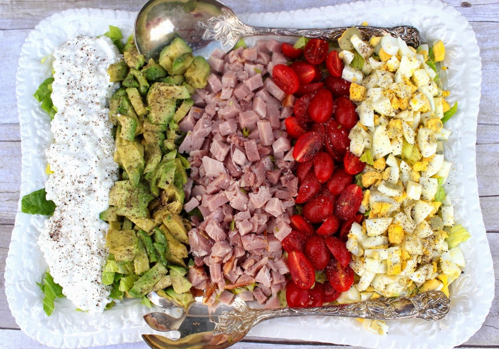 A colorful Cobb Salad with rows of egg, tomato, ham, avocado, and cottage cheese.