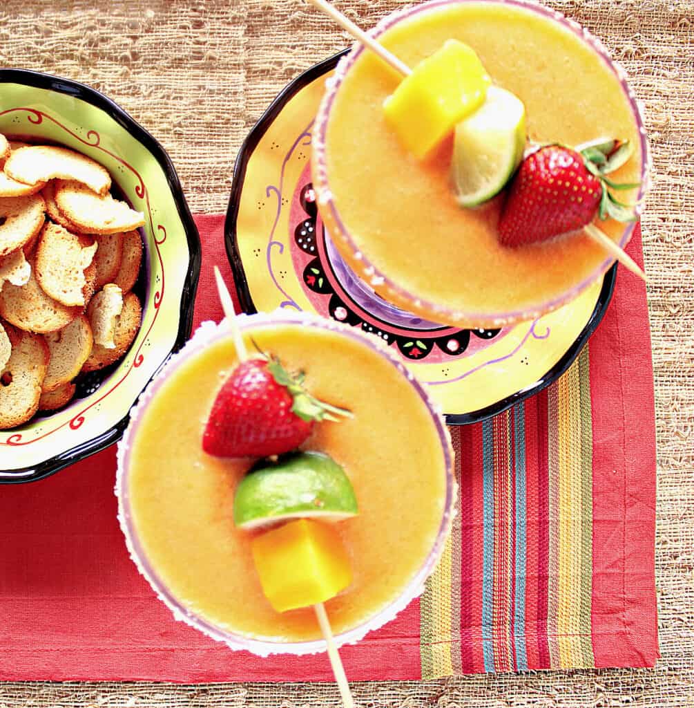 An overhead photo of two Frozen Mango Strawberry Margarita's with salted rims and fresh fruit garnish.