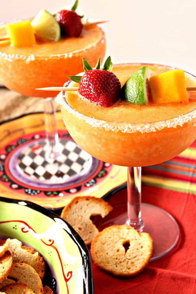 A vertical closeup of two delicious Frozen Mango Strawberry Margaritas in salt-rimmed glassed with fresh fruit as garnish.