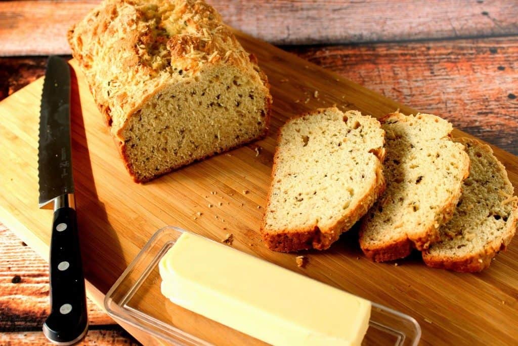 Sliced Homemade Soda Bread on a cutting board with a serrated knife and butter in a dish.