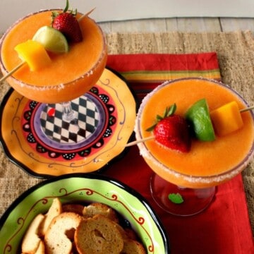 Two Frozen Strawberry Mango Margaritas in large cocktail glasses with mango, strawberry, and lime on skewers.