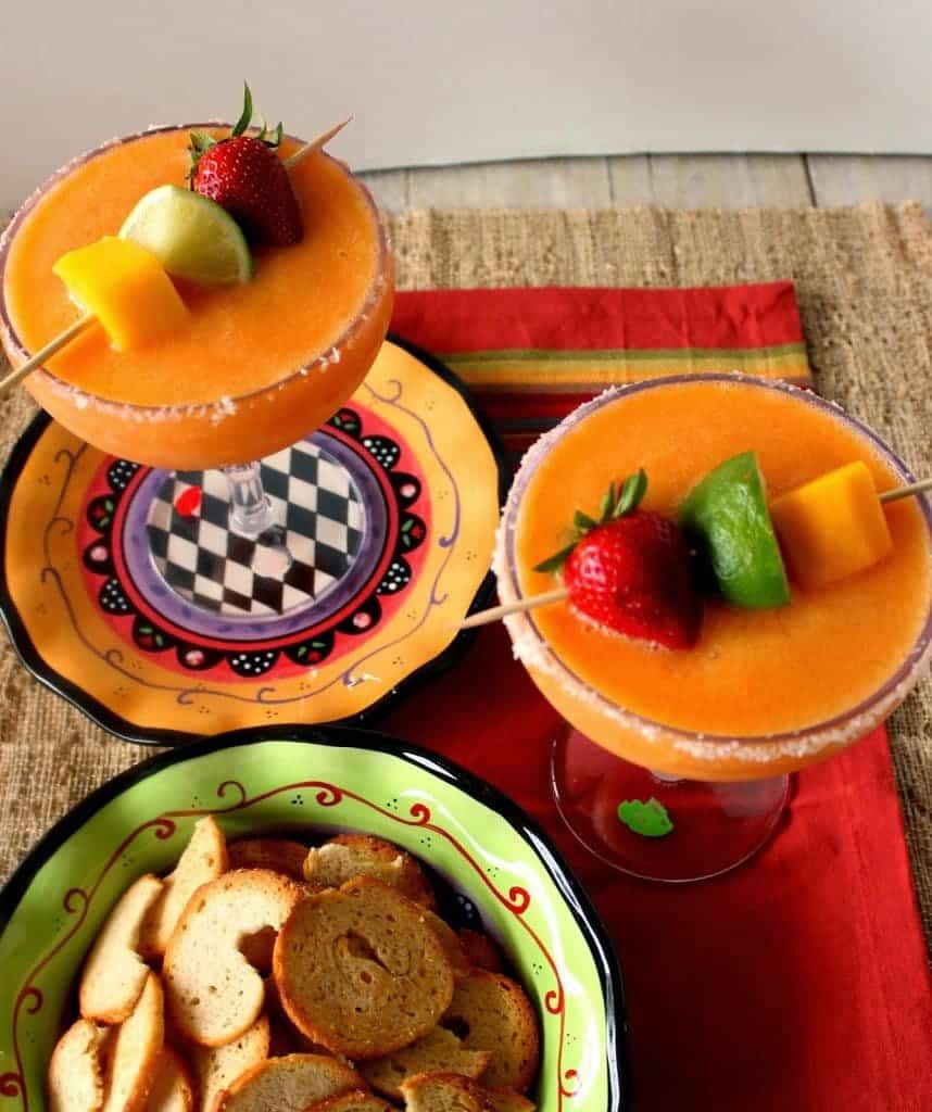 Two Frozen Strawberry Mango Margaritas in large cocktail glasses with mango, strawberry, and lime on skewers.