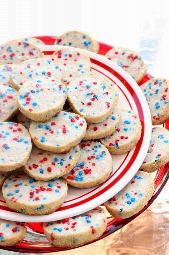 A closeup vertical photo of a bunch of red white and blue cream cheese cookies on a tiered cookie platter.