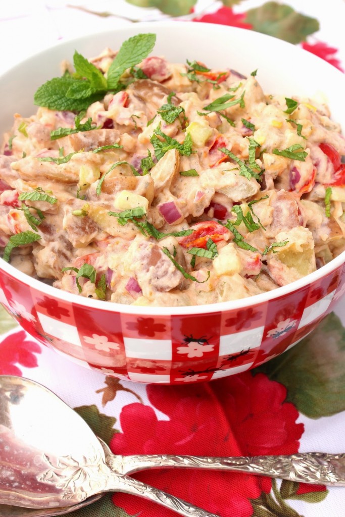 A large red and white checkered bowl filled with Tzatziki Potato Salad and topped with mint.