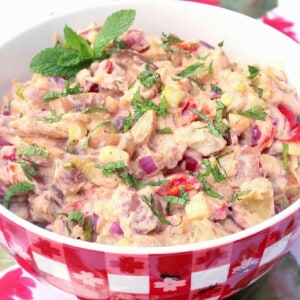 A large red and white checkered bowl filled with Tzatziki Potato Salad and topped with mint.