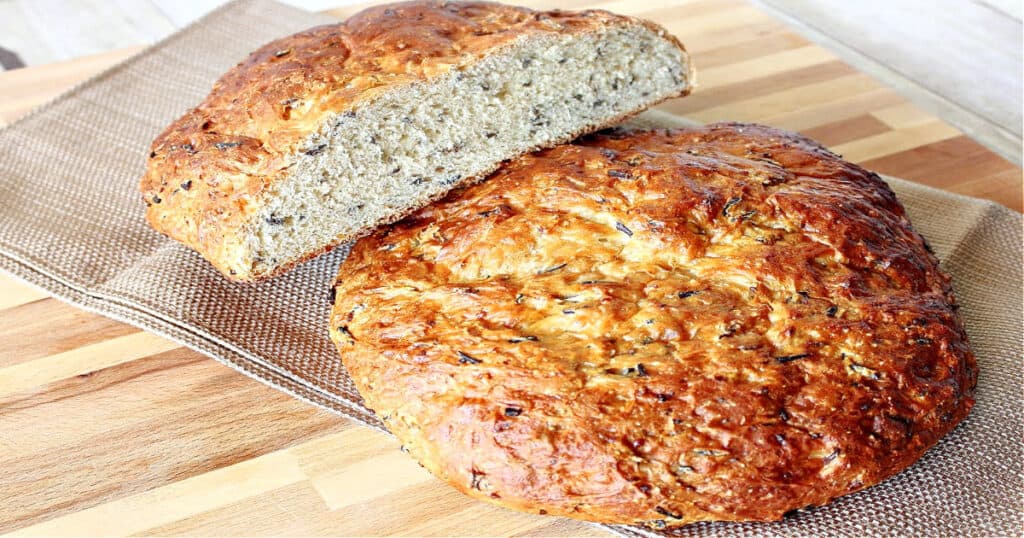 Two rustic loaves of Wild Rice Bread with Onions on a wooden board with a napkin.