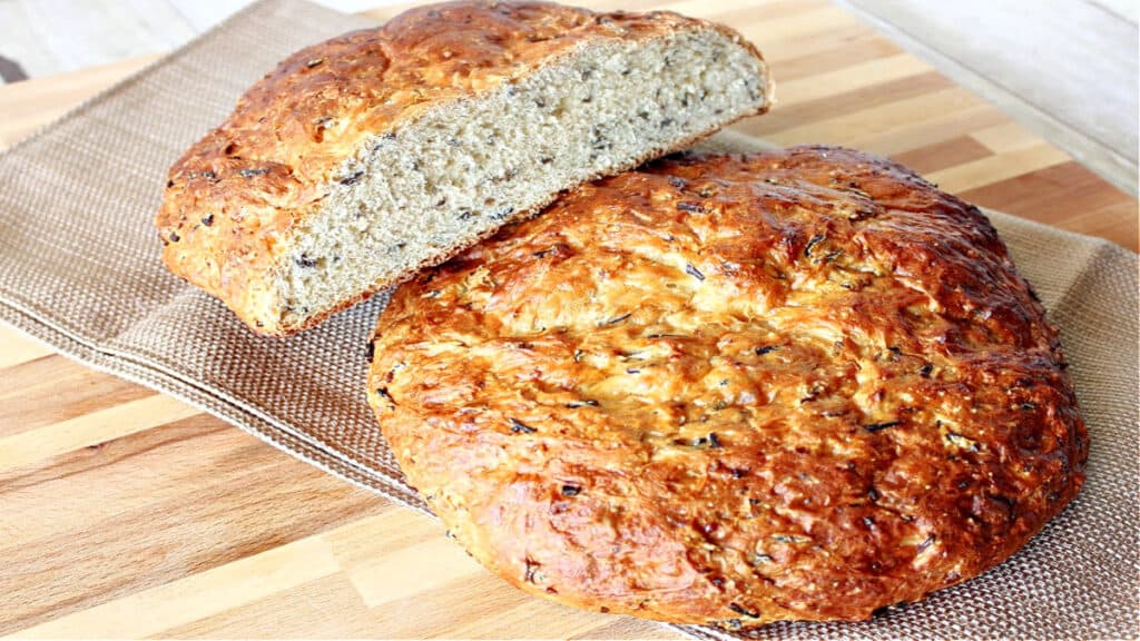 Two rustic loaves of Wild Rice Bread with Onions on a wooden board with a napkin.