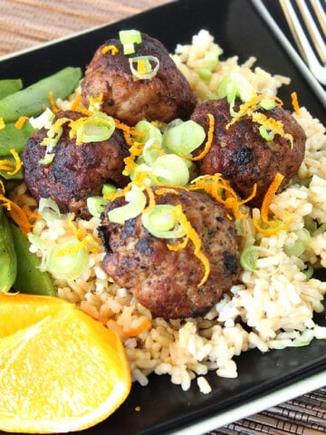 Asian Pork Meatballs on a black square plate with pea pods and orange wedges.