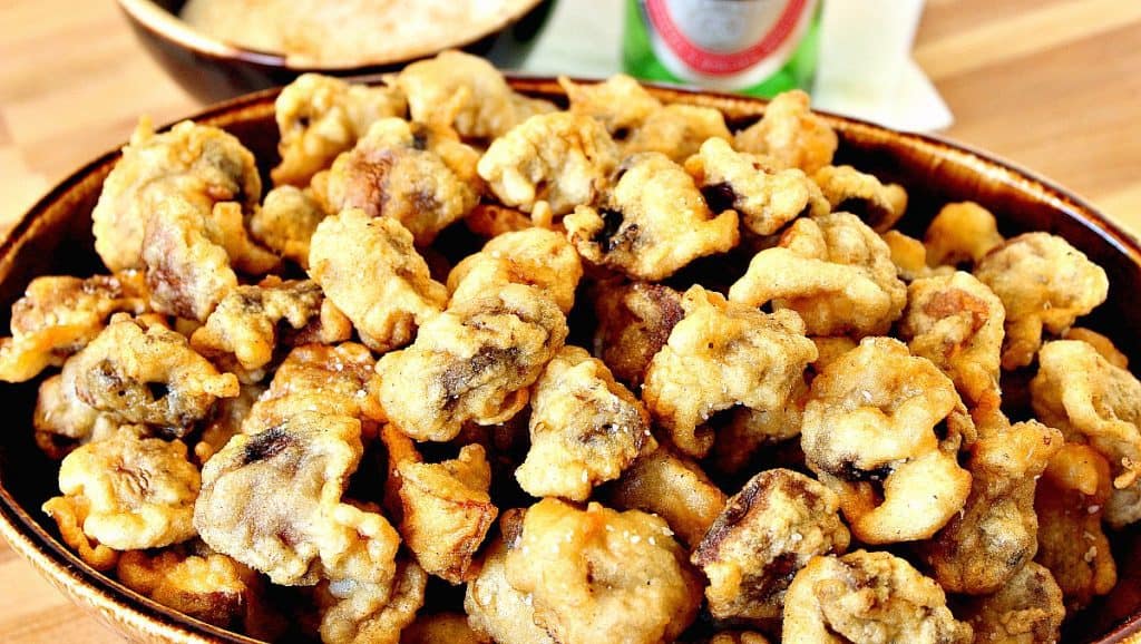 A horizontal photo of a large brown oval bowl filled with golden fried mushrooms.