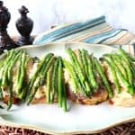 Chicken Oscar on a platter with asparagus spears and a blue and tan striped napkin