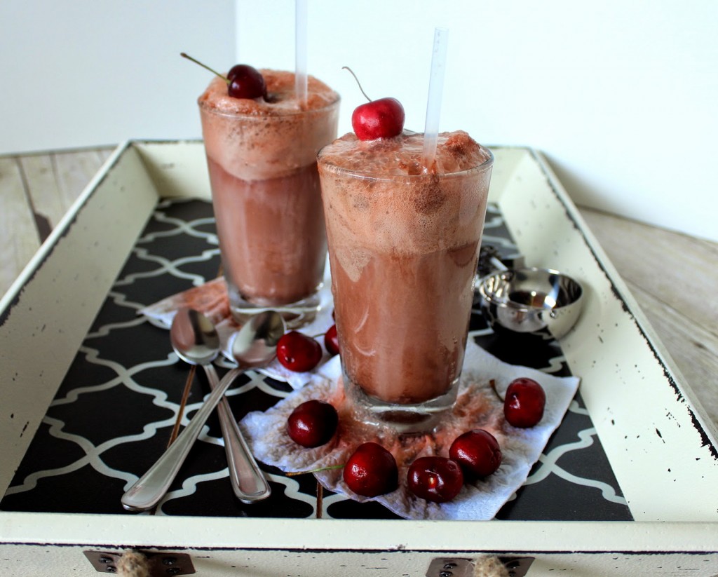 Two tall glasses of Chocolate Cherry Cows on a tray with straws and cherries.