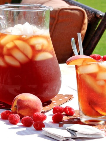 A pitcher and glass filled with ice and Peach and Raspberry Sun Tea.