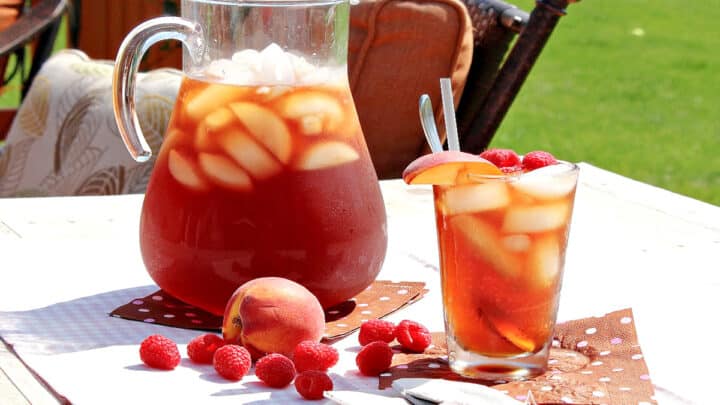A pitcher and glass filled with ice and Peach and Raspberry Sun Tea.