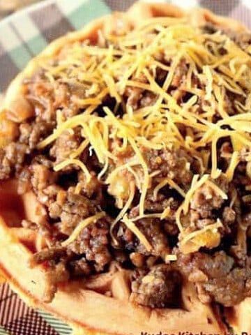 A serving of Sloppy Joe over Cornbread Waffles with shredded cheese on top.