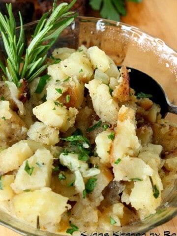 A glass bowl filled with Grilled Rosemary Potatoes along with a sprig of fresh rosemary.