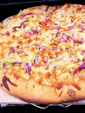 A Buffalo Chicken Pizza on a pizza stone on and outdoor grill.