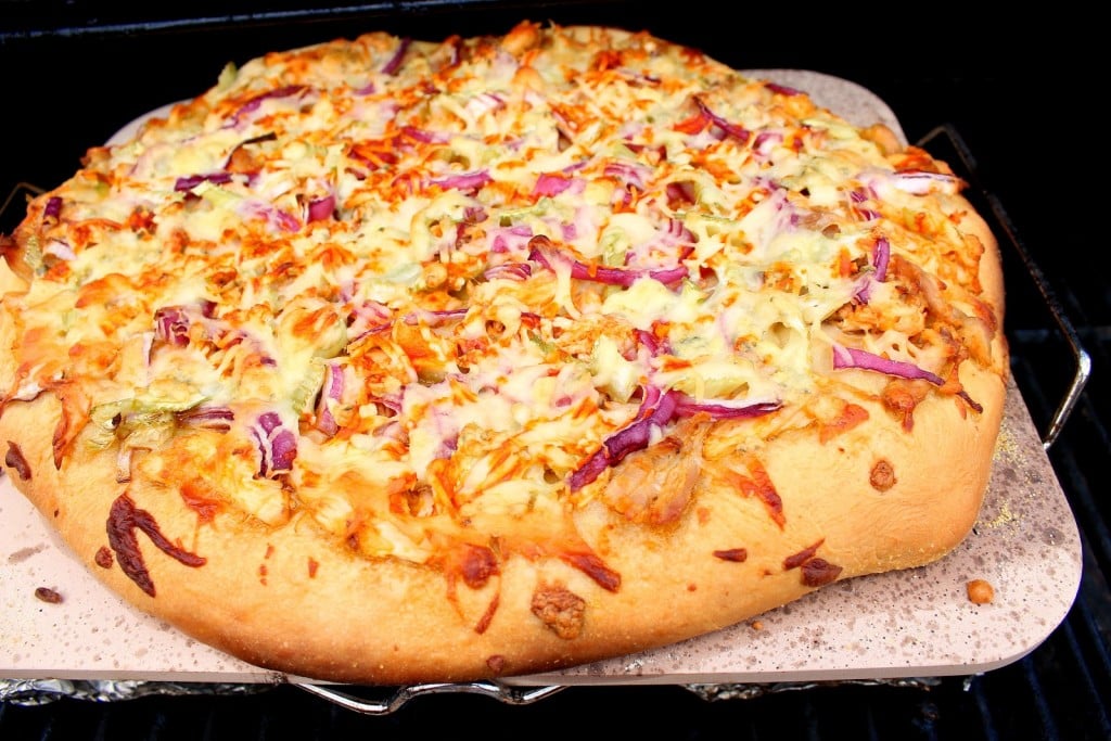 A Buffalo Chicken Pizza on a pizza stone on and outdoor grill.