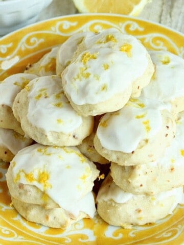 A yellow and white plate stacked with Lemon Ricotta Cookies with white icing.