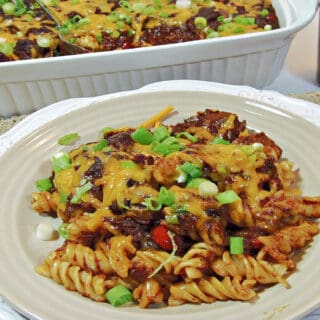 A white plate in the foreground filled with Mexican Mac and Cheese along with green onions.