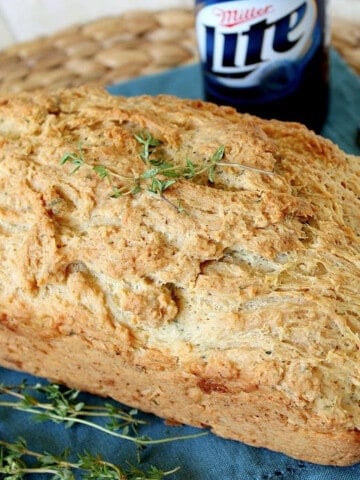 A loaf of Beer Bread with Thyme along with a bottle of beer in the background.