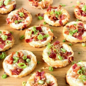 A bunch of round Cheese and Bacon Tarts on a wooden board topped with scallions