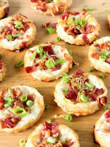 A bunch of round Cheese and Bacon Tarts on a wooden board topped with scallions