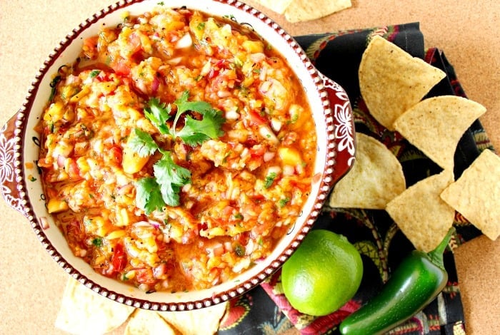 Overhead photo of a bowl of peach salsa with chips and a lime.