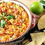 Fresh peach salsa in a bowl with cilantro, chips, lime and jalapeno