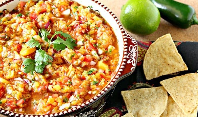Fresh peach salsa in a bowl with cilantro, chips, lime and jalapeno