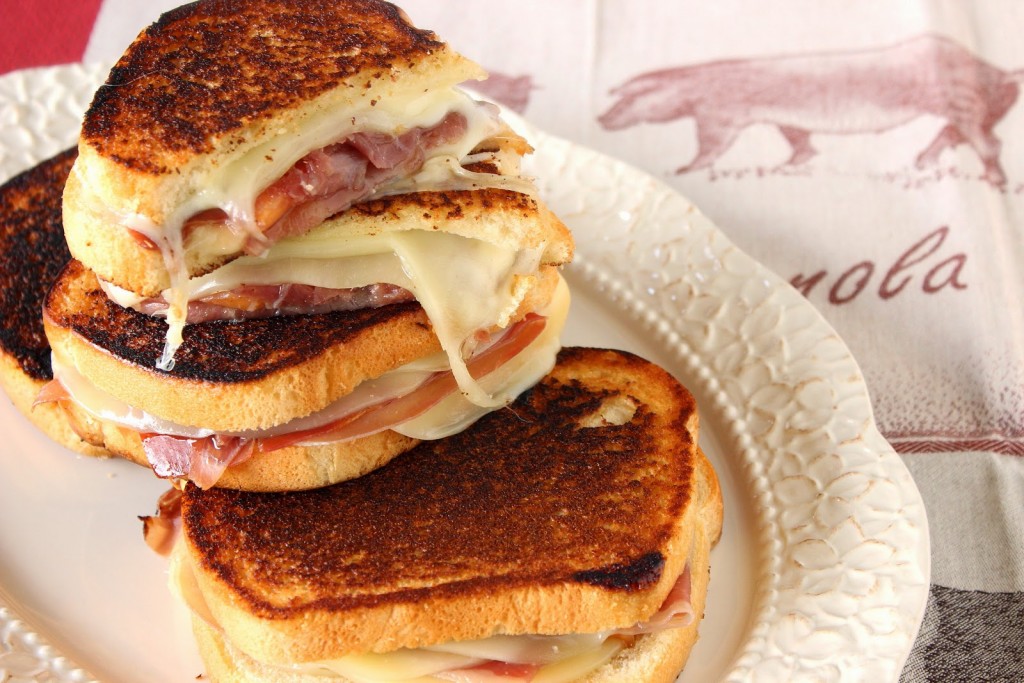 A horizontal photo of several halved prosciutto, melon, and provolone grilled cheese sandwiches on an oval platter.