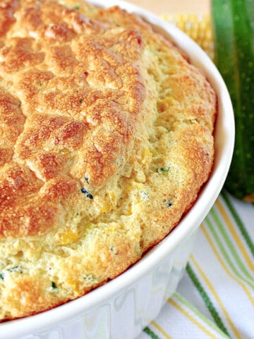 A horizontal offset photo of a Zucchini and Sweet Corn Souffle in a dish on a stripped green and yellow napkin.