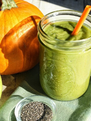 A green Fall Harvest Smoothie in a mason jar with an orange straw