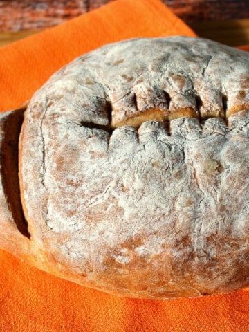 A football shaped loaf of French bread on an orange cloth napkin.