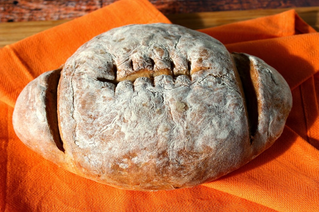 A loaf of shaped French Bread Football on an orange cloth napkin.
