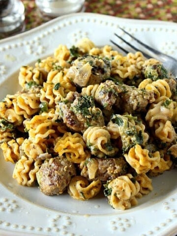 A serving of Pumpkin and Sausage Pasta with spinach and fork on a plate.