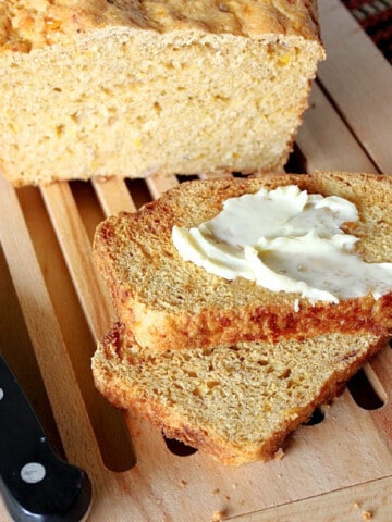 A loaf of Southwestern Cornbread on a wooden bread board with a knife.