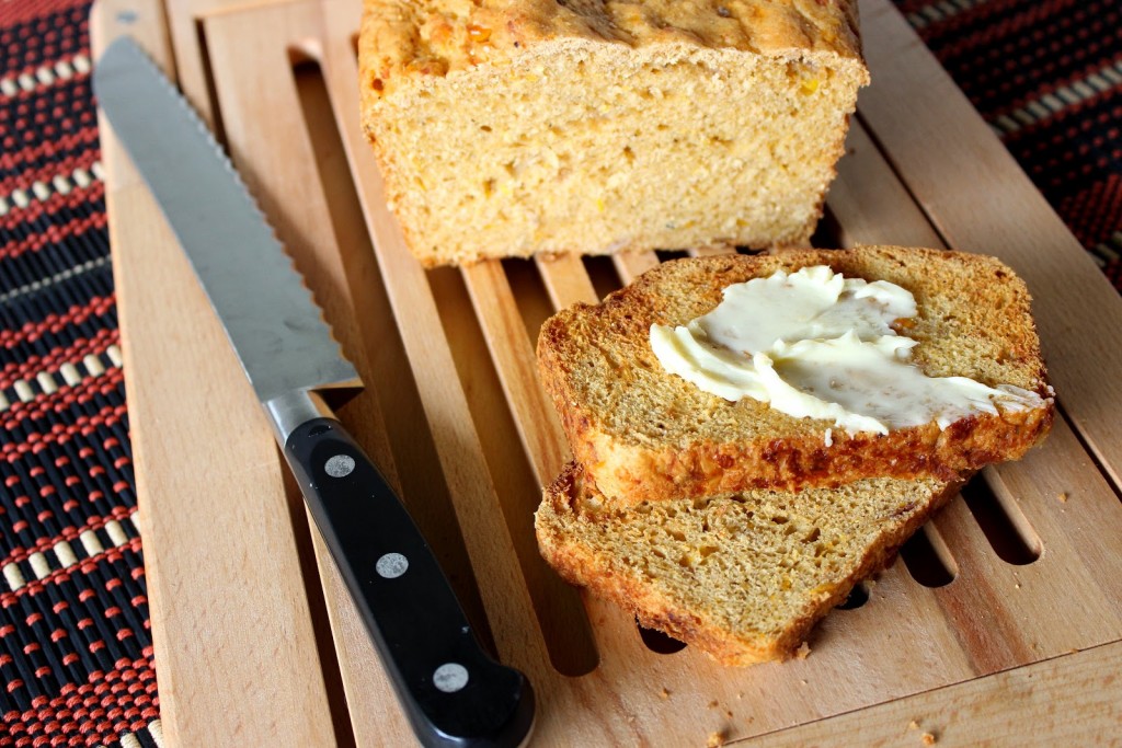A loaf of Southwestern Cornbread on a wooden bread board with a knife.