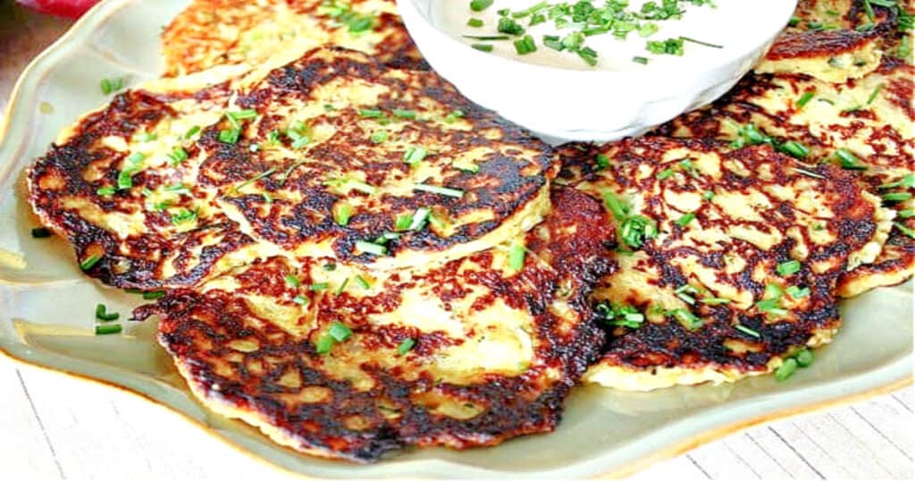 A plate filled with fried Spaghetti Squash and Zucchini Pancakes with chives as garnish.