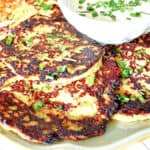 A plate filled with fried Spaghetti Squash and Zucchini Pancakes with chives as garnish.