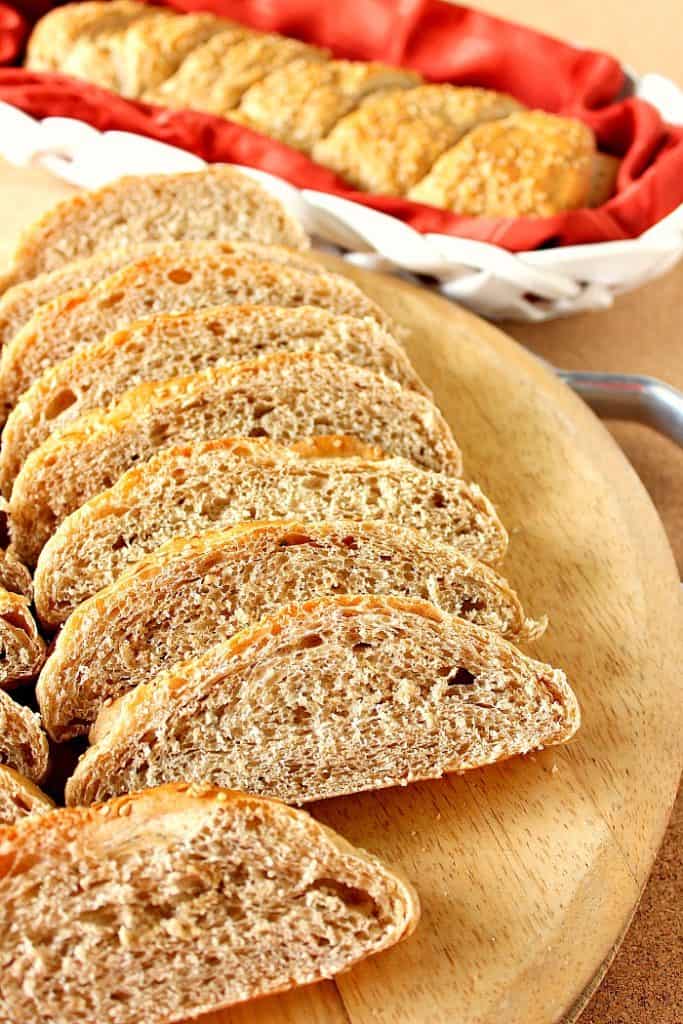 Vertical photo of slices of whole wheat French bread on a cutting board with a whole loaf in the background.