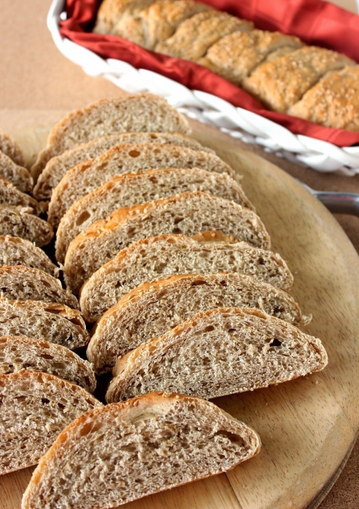 Vertical image of sliced whole wheat French bread on a cutting board.